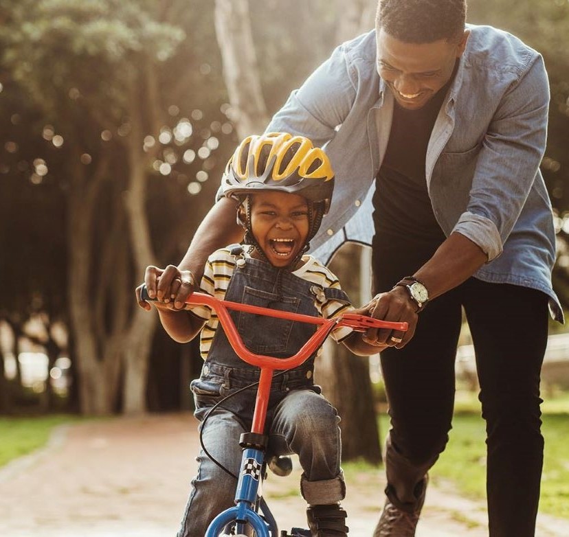 Boy learning to ride a bicycle with his father in the park.